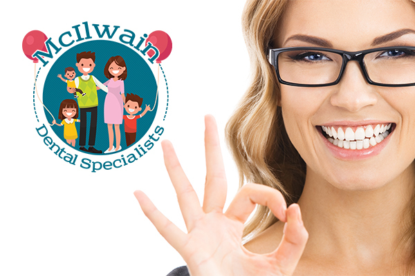 Woman wearing glasses and smiling while signaling OK with her hand next to a logo of McIlwain Dental Specialists.