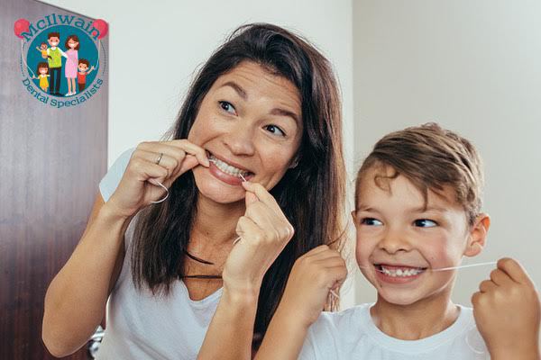 Two individuals flossing their teeth while smiling next to a logo of McIlwain Dental Specialists.