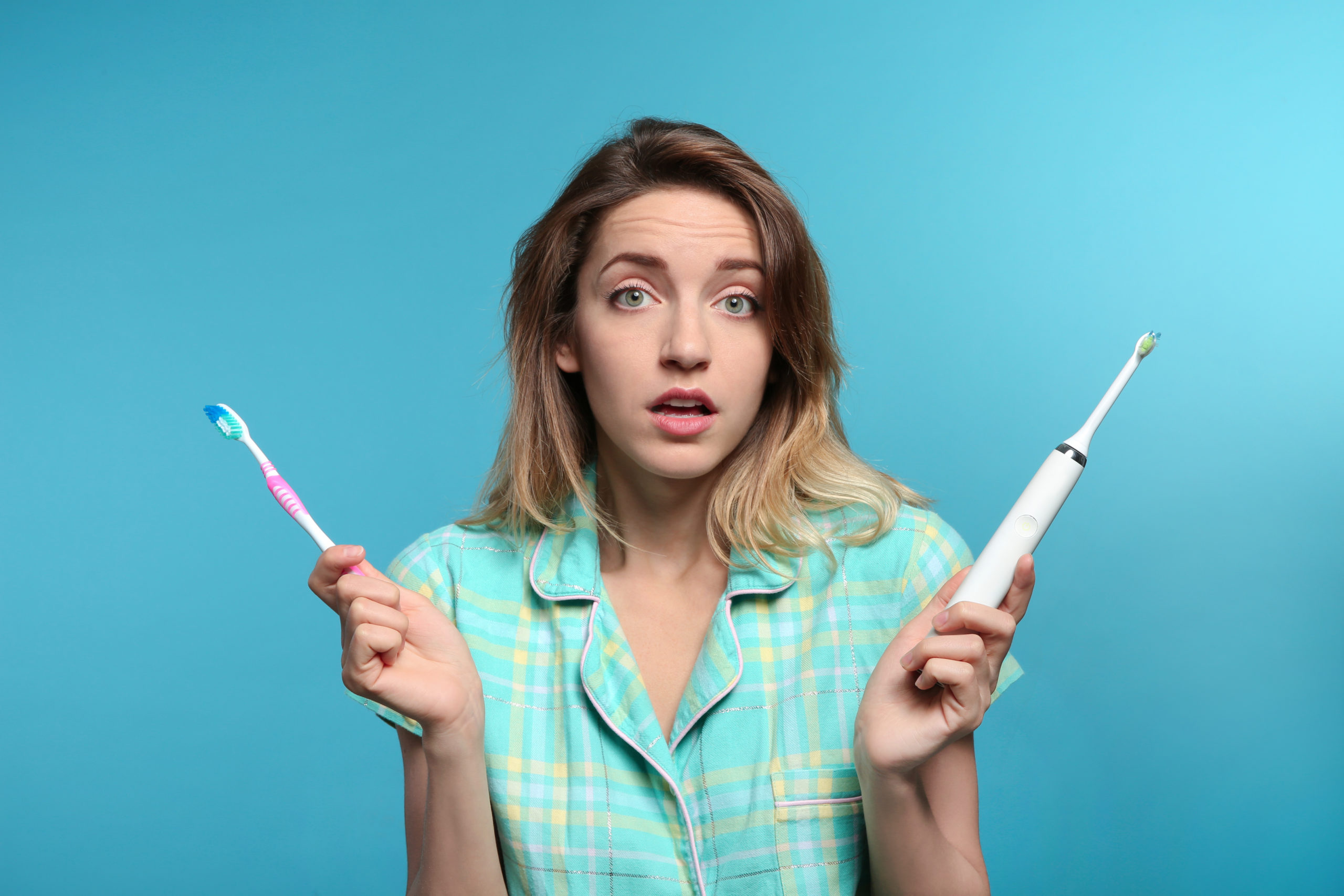 Woman holding a traditional toothbrush and an electric toothbrush on a blue background.