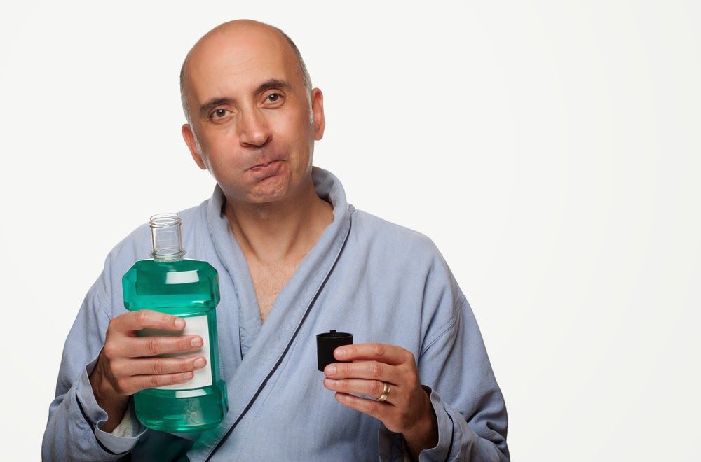 Man holding mouthwash while wearing a robe with a white background.