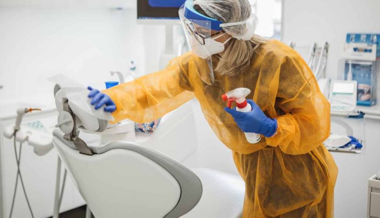 Person wearing protective gear cleaning a dental chair in a dental clinic.