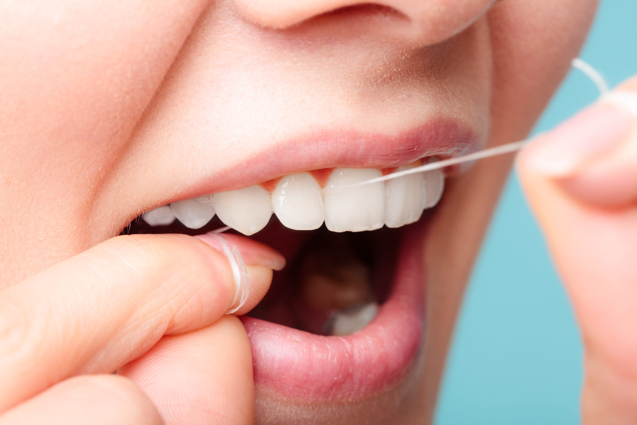 Close-up of a person flossing their teeth on a blue background.