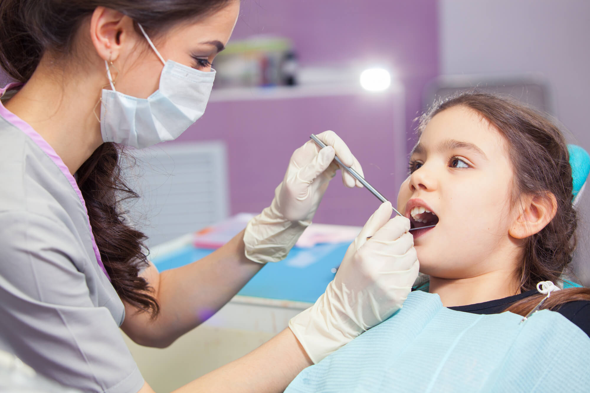 Dentist in gloves holding dental instruments near a patient in a clinic.