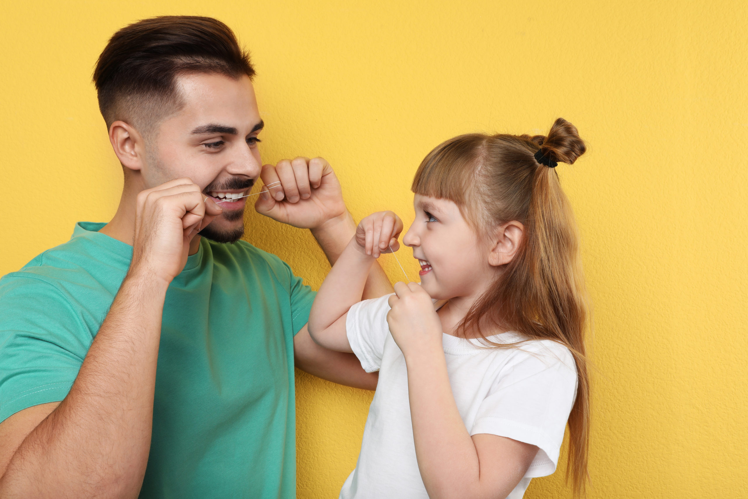 A little girl and her father flossing their teeth together while smiling