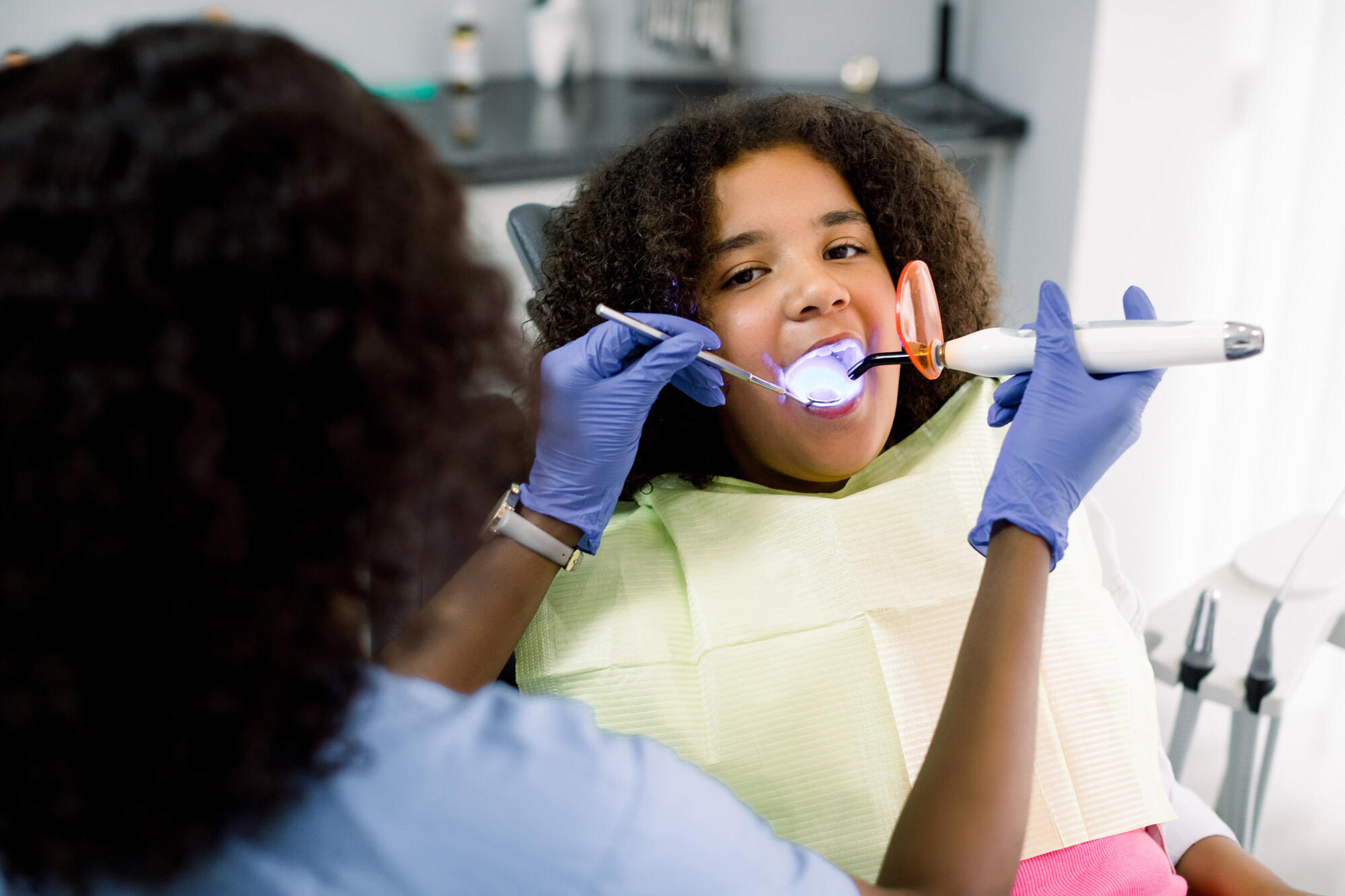 Little girl in dental chair with dentist looking at teeth