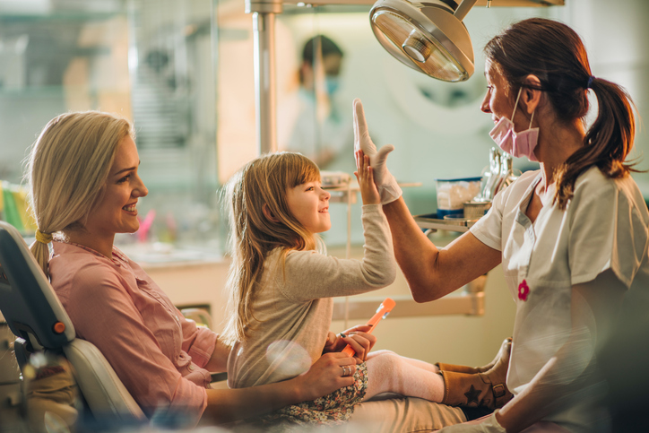 Happy girl with her mother giving high five to a dentist after medical exam at dentist's office.