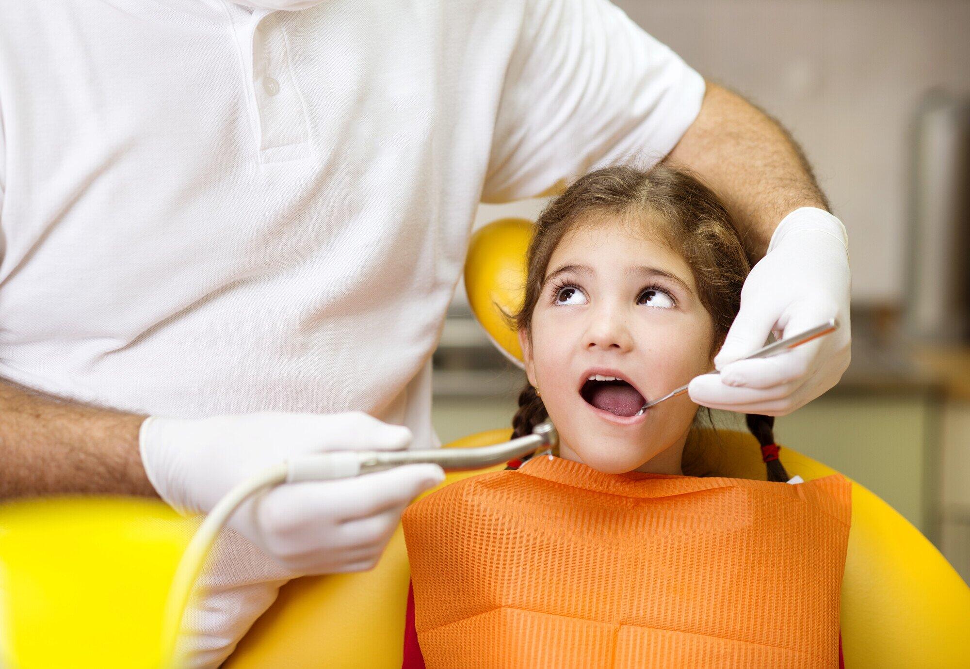 Small child in a yellow dental chair having teeth examined.