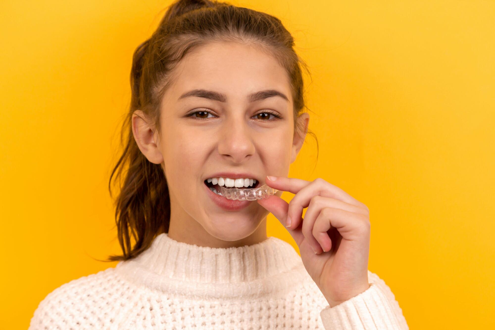 Young girl in a cream sweater putting in Invisalign