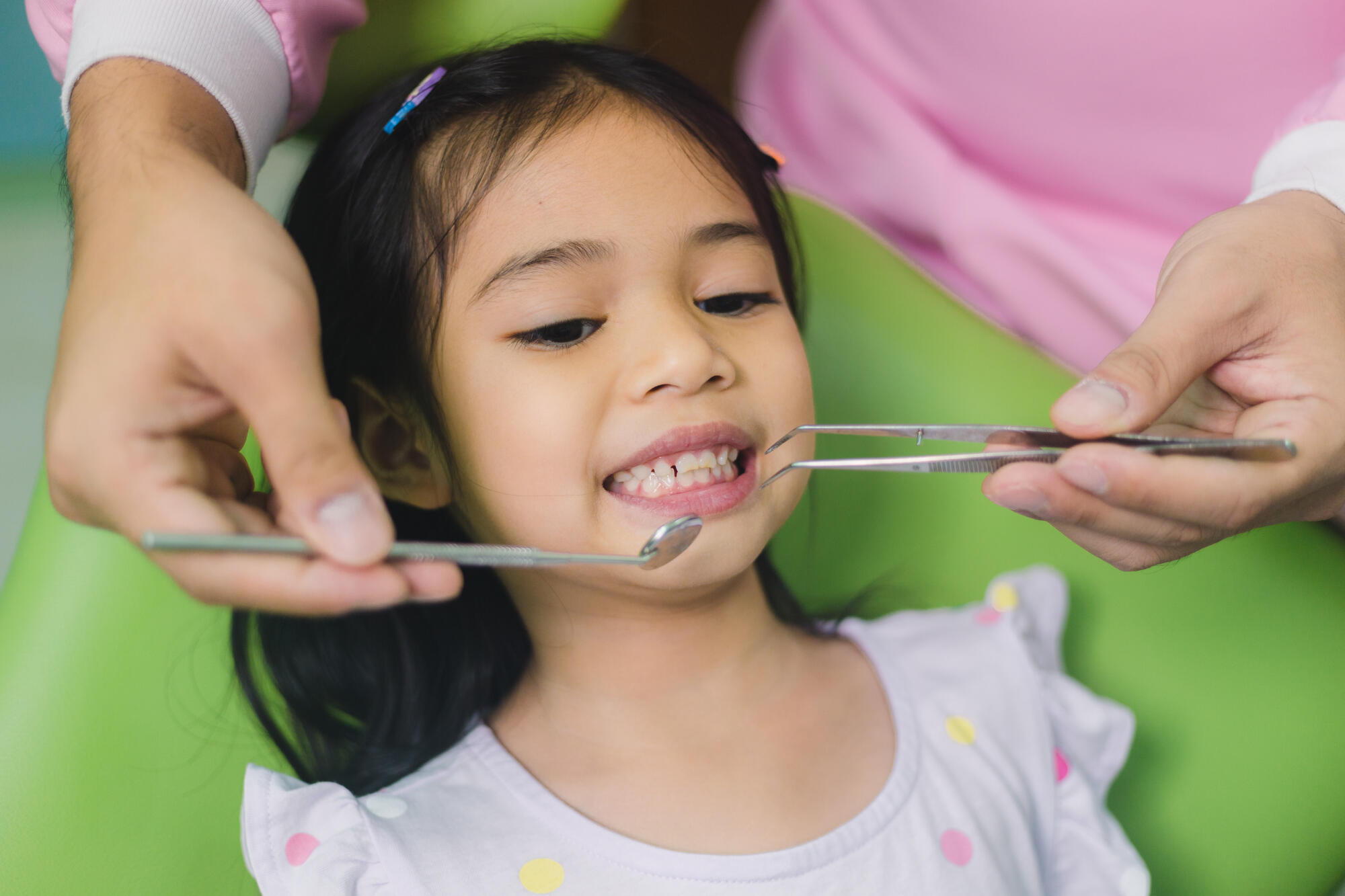 Small girl sitting in a green dental chair having teeth examined.